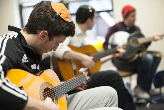 Three men sitting in a row play guitars